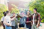 Happy male friends toasting drinks over barbecue grill in backyard