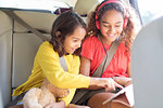 Sisters using digital tablet in back seat of car