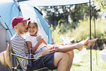 Happy, affectionate father holding daughter in lap at sunny campsite