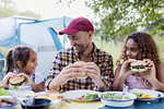 Father and daughters enjoying barbecue hamburger lunch at campsite