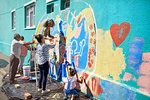 Community volunteers painting multicolor mural on sunny urban wall