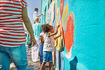 Girl volunteer painting vibrant mural on sunny wall