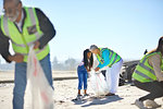Senior woman and girl volunteer cleaning up litter on sunny, sandy beach