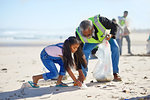 Grandfather and granddaughter volunteers cleaning up litter on sunny, sandy beach