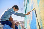 Father and son volunteers painting mural on sunny wall