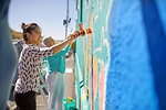 Women painting vibrant mural on sunny urban wall