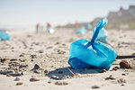 Blue bag of litter on sunny, sandy beach