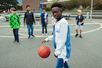 Portrait confident tween boy playing basketball in schoolyard