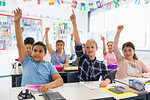 Eager junior high school students with hands raised in classroom