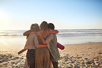 Female friends with yoga mats hugging on sunny beach