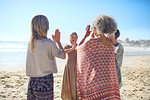 Women friends with hands clasped in circle on sunny beach during yoga retreat