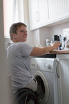 Young woman in wheelchair preparing tea in apartment kitchen