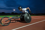 Determined young male paraplegic athlete speeding along sports track in wheelchair race at night