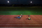 Paraplegic athletes speeding along sports track in wheelchair race at night