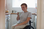 Portrait smiling, confident young woman in wheelchair drinking tea in apartment kitchen