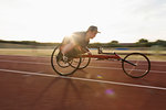 Determined teenage boy paraplegic athlete speeding along sports track in wheelchair race