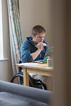 Focused young woman in wheelchair using laptop at dining table