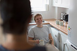 Happy young woman in wheelchair drinking tea in apartment kitchen