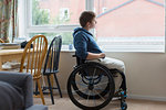 Thoughtful young woman in wheelchair looking out window