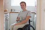 Portrait confident young woman in wheelchair drinking tea in apartment kitchen