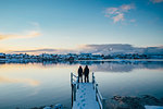 Couple holding hands at the edge of snowy dock overlooking waterfront village, Reine, Lofoten Islands, Norway