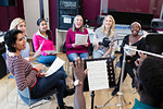 Male conductor leading womens choir with sheet music singing in music recording studio