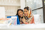 Happy mother in hijab and daughter using laptop