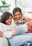 Laughing, happy mother in hijab and daughter using digital tablet