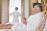 Mature man in spa bathrobe using digital tablet on hotel bed