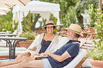Mature couple reading books, relaxing on lounge chairs at resort poolside