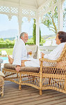 Mature couple in bathrobes relaxing, drinking champagne in resort gazebo