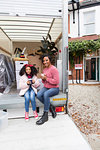 Portrait happy mother and daughter drinking tea, taking a break at back of moving van outside new house