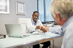 Male doctor shaking hands with senior patient in doctors office