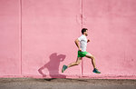 Young male runner running past pink wall