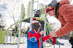 Father putting on boy's gloves by playground slide in snow