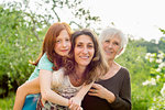 Girl getting piggyback with mother and grandmother in garden, portrait