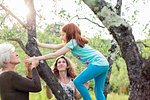 Girl climbing garden tree, watched by mother and grandmother