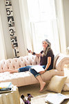 Stylish mature woman sitting on sofa holding smartphone, portrait