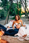 Bride and groom reclining by campfire on lakeside