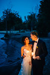 Romantic bride and groom with sparklers strolling on lakeside at dusk