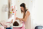 Mother changing baby girl's diaper on changing table