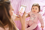 Mother taking photograph of baby girl on bed