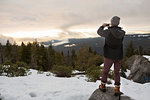 Mid adult man photographing view from rock on snow covered mountain, rear view, Twain Harte, California, USA