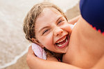 Laughing girl being hugged by mother on beach, Portoferraio, Tuscany, Italy