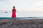 Girl in red dress watching sea from beach, rear view, Portoferraio, Tuscany, Italy