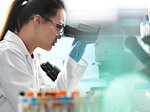 Scientist viewing human sample on glass slide with microscope in laboratory