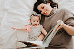 Mother reading with baby daughter on bed