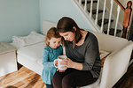 Female toddler and mother looking at coffee cup on sofa