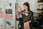 Mother carrying baby son drying dishes in kitchen