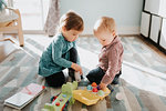 Female toddler playing with baby brother in living room